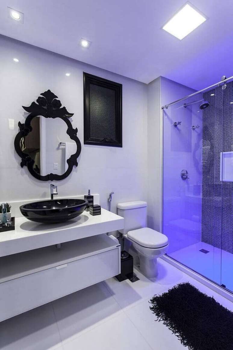 7. Esse banheiro branco é um modelo de banheiro com cerâmica preta e branca que recebeu detalhes modernos e clássicos como o espelho provençal e a bancada com linhas simples.