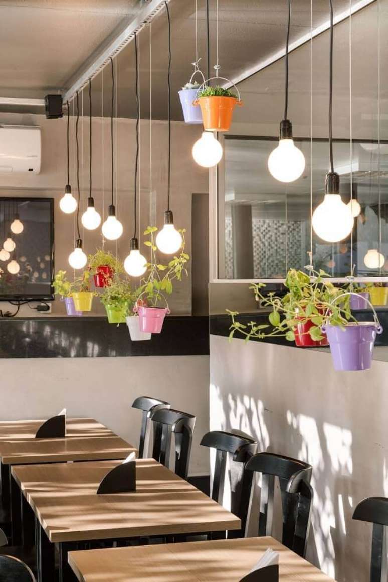 25. Esse restaurante utilizou vasoso decorativos coloridos e suspensos sobre a mesa criando um ambiente divertido e alegre