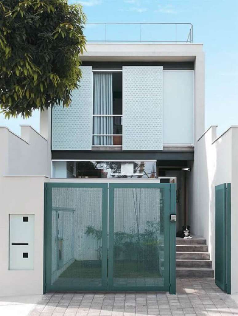 6. Frente de casas com muito e portão verde, com uma arquitetura simples, porém, bonita.