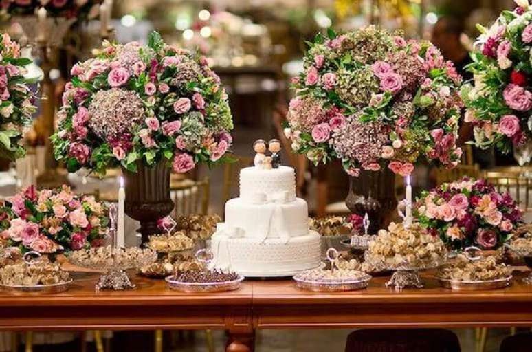 21. Decoração de mesa de casamento bem clássica com muitas flores e bolo branco