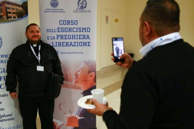 Um padre posa para fotos próximo ao banner do Curso de Exorcismo. (Foto: Reuters)