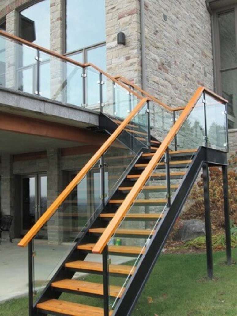 43. Escada com estrutura de ferro e degraus e corrimão de madeira com guarda-corpo de vidro