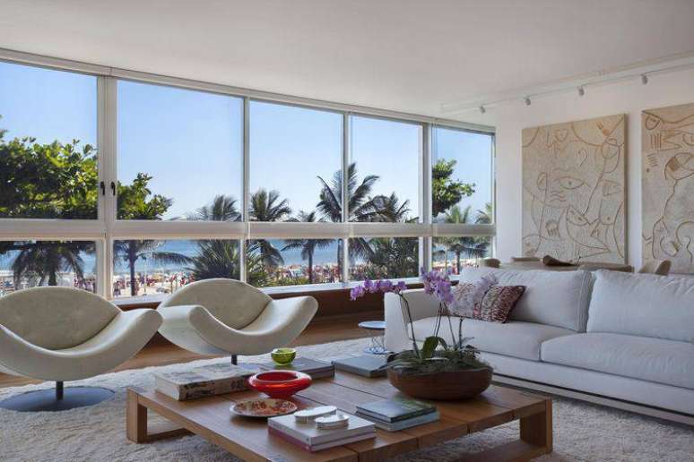 37. Sala decorada com m&oacute;veis claro e com uma bela vista para o mar