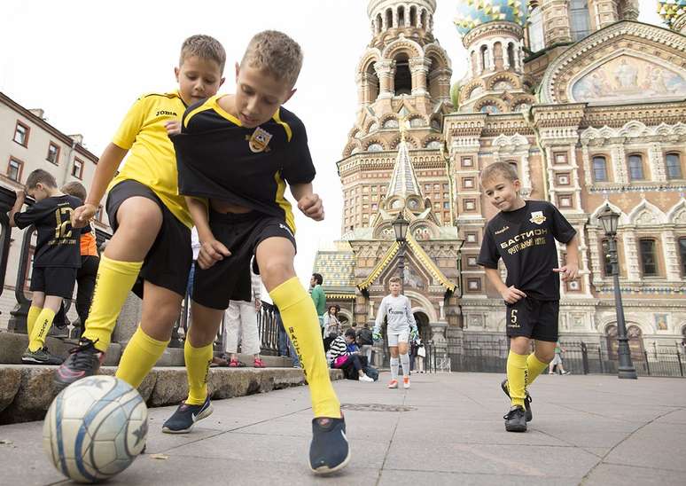 Garotos 'atrapalham o movimento' no passeio público jogando bola em frente à Catedral do Sangue Derramado em São Petersburgo, antiga capital do Império Russo, onde Pushkin, Dostoievsky, Gogol e outros autores ambientaram algumas de suas obras