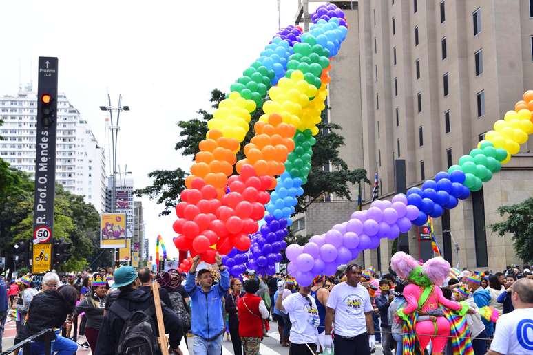 A multidão, fantasiada, com coroas com as cores do arco-íris e fantasias de Carnaval, se amontoa ao redor dos 18 trios elétricos enfileirados pela avenida