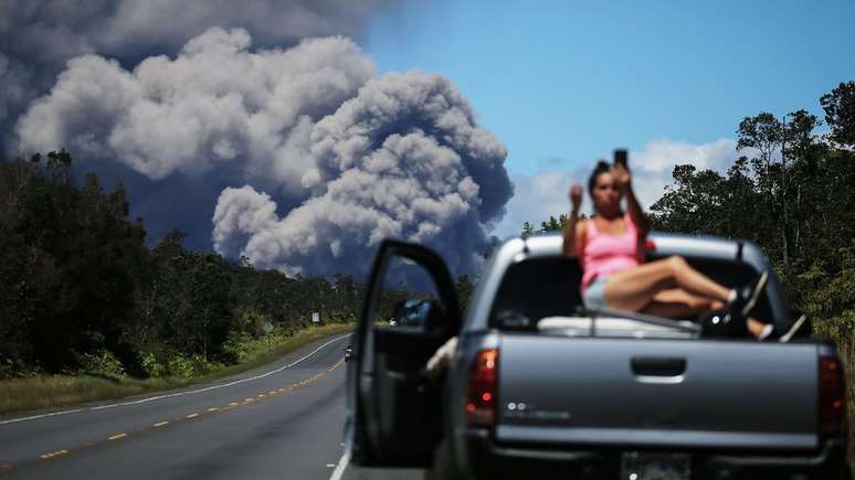 Mulher faz selfie com o vulc&atilde;o Kilauea ao fundo; apesar de incontrol&aacute;veis, erup&ccedil;&otilde;es vulc&acirc;nicas n&atilde;o resultam sempre em morte e desastre