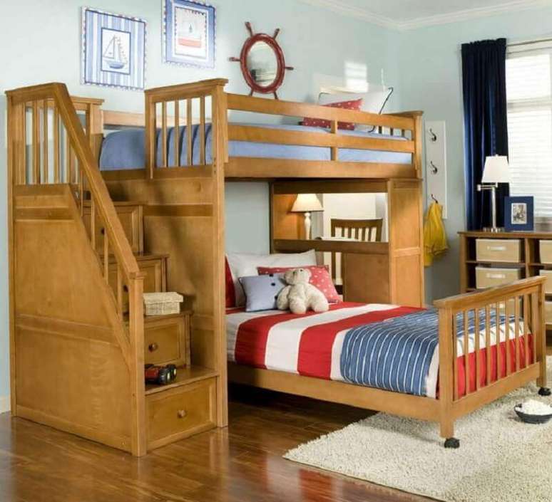 48. Nesse quarto decorado com beliche com escrivaninha de madeira também possui uma cama extra com rodinhas