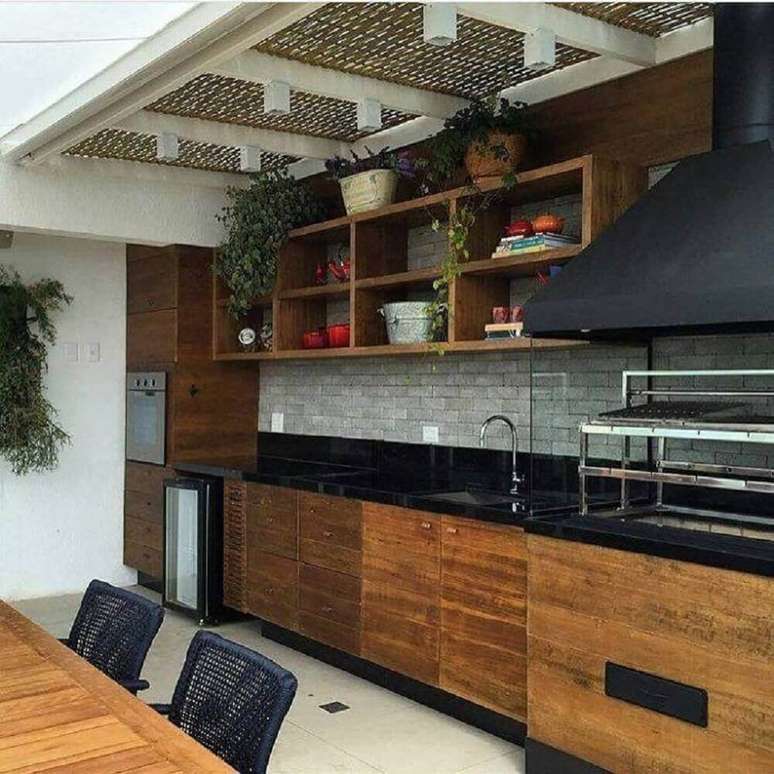 20. Cozinha com granito preto absoluto e armários de madeira, o toque moderno ficou por conta dos tijolinhos cinza na parede