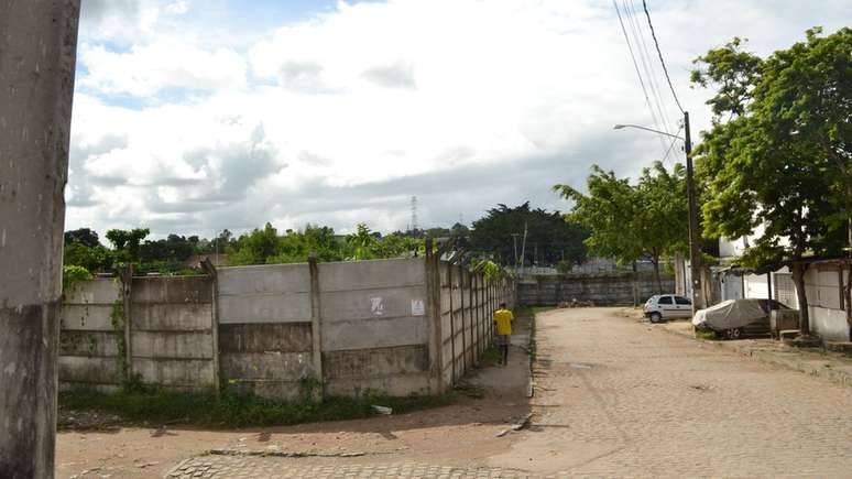 Terreno baldio deixado no Loteamento São Francisco após as desapropriações foi cercado de um muro, e tem sido usado para armazenar ônibus de uma empresa de transportes privada / Crédito: Lara Salviano e Gabriela Passos/Universidade Católica de Pernambuco