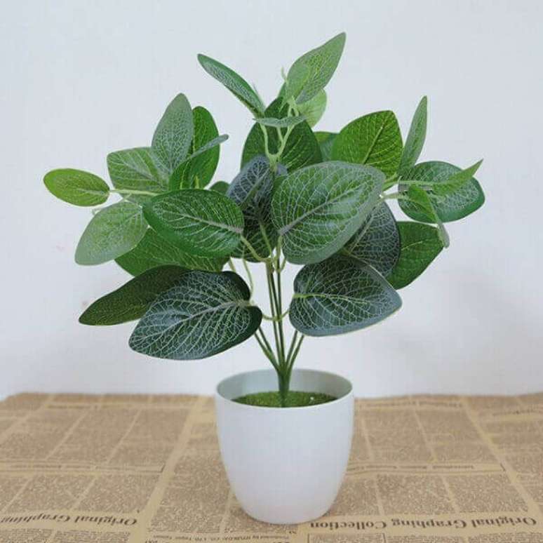 25 &ndash; Planta artificial com folhas verdes escuras.