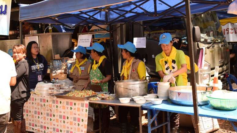 Voluntários e funcionários da cozinha real tailandesa preparam refeições para todos no acampamento da operação de resgate