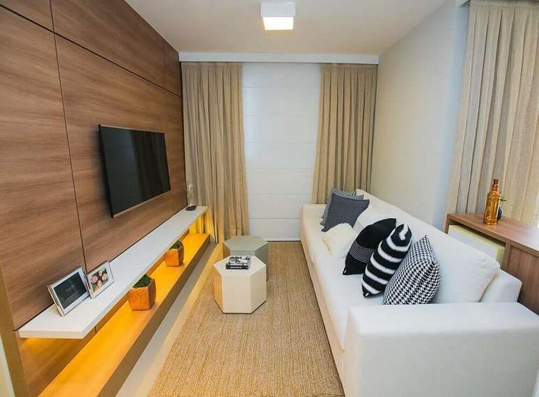 59. Sala de estar moderna e pequena decorada na cor bege claro com painel de madeira para televisão