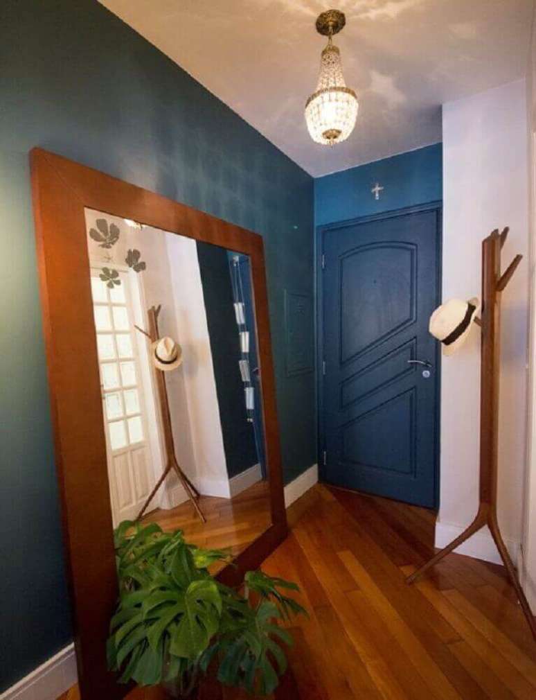 33. Hall de entrada de apartamento pequeno decorado com espelho apoiado no chão e paredes pintadas de azul