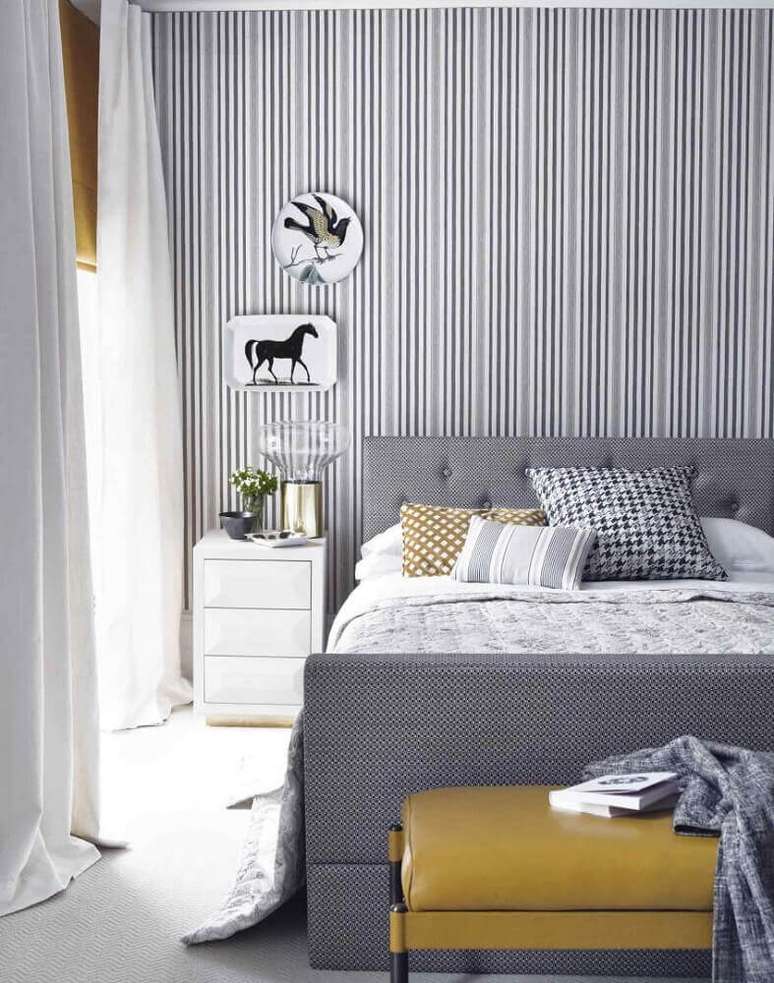 40. Decoração para quarto de casal moderno em tons de cinza com papel de parede listrado e quadros acima do criado mudo