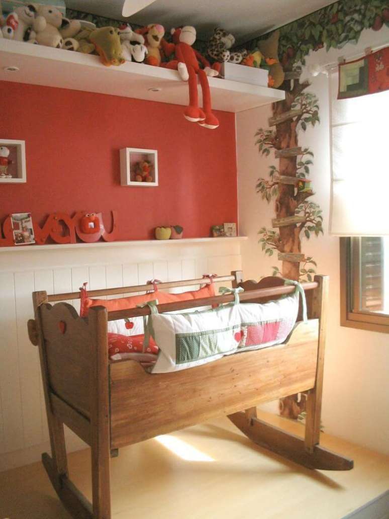 41. O tema de natureza desta decoração de quarto de bebê traz uma parede em vermelho e pintura de árvore, além do berço retrô em madeira. Projeto de Le Saldanha