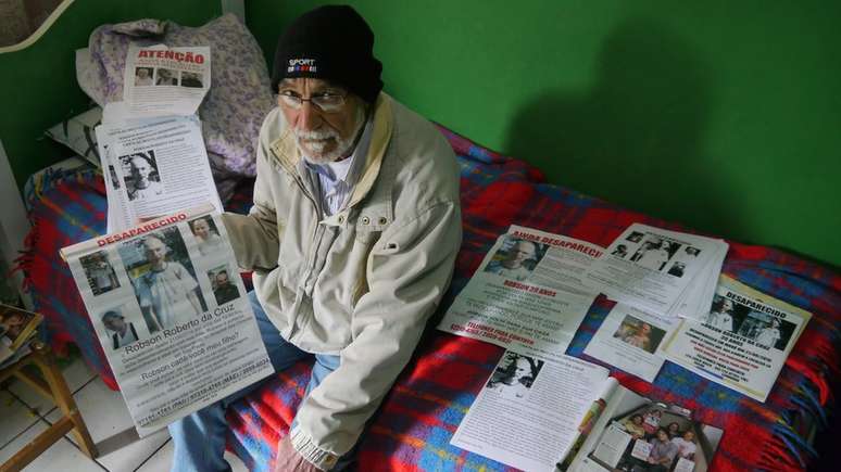 Leonardo da Cruz, pai de Robson, ao lado de sete tipos diferentes de cartazes que colou pela Grande S&atilde;o Paulo em busca do filho