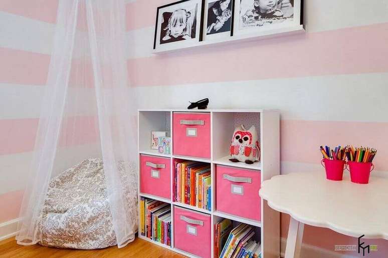 44. Cantinho da leitura para criança decorado em tons de rosa com papel de parede listrado, estante baixa e puff grande redondo – Foto: Gosia Design