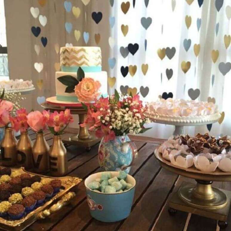 11- A decora&ccedil;&atilde;o de noivado tem arranjo de cora&ccedil;&otilde;es pendurados atr&aacute;s da mesa. Fonte: Canal da decora&ccedil;&atilde;o