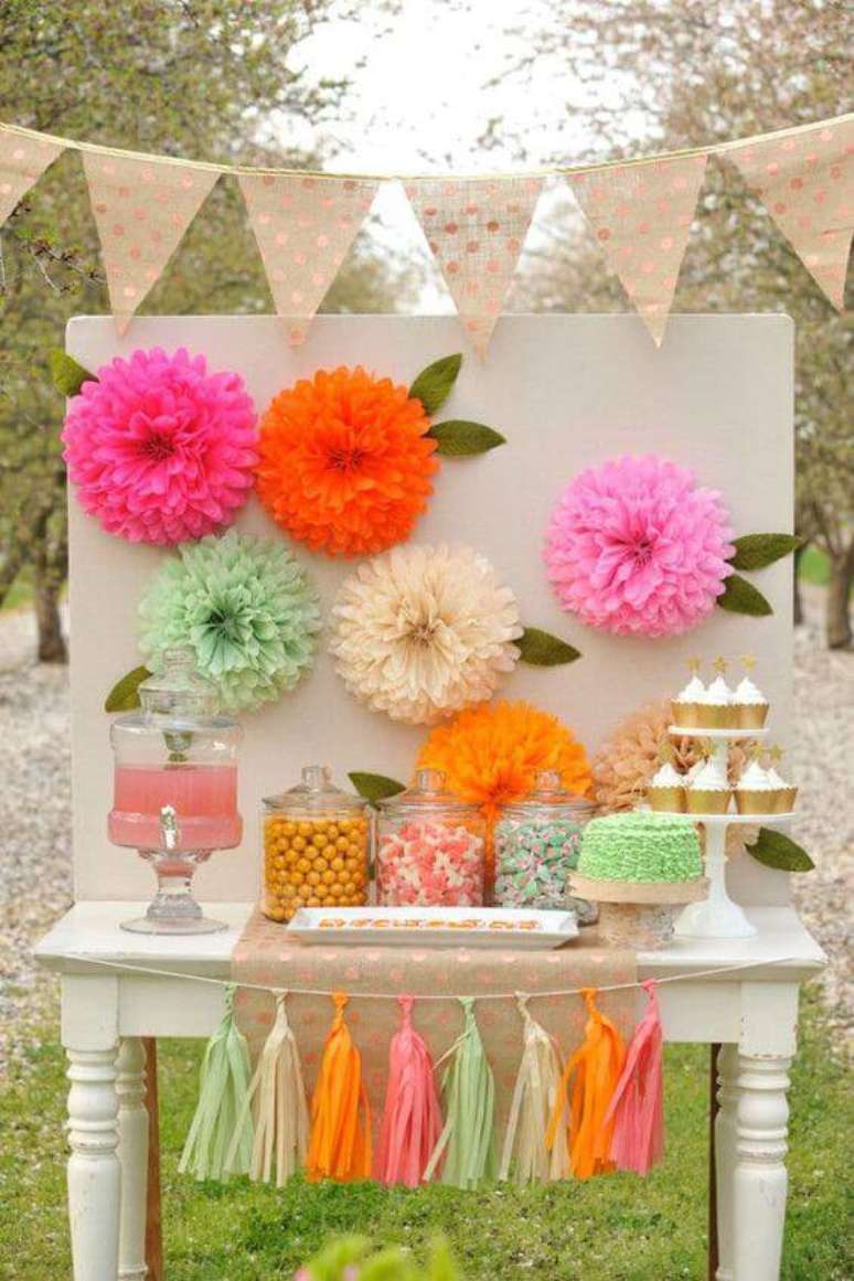 29. A decoração de festa com flores e enfeites de papel fica bonita e colorida.