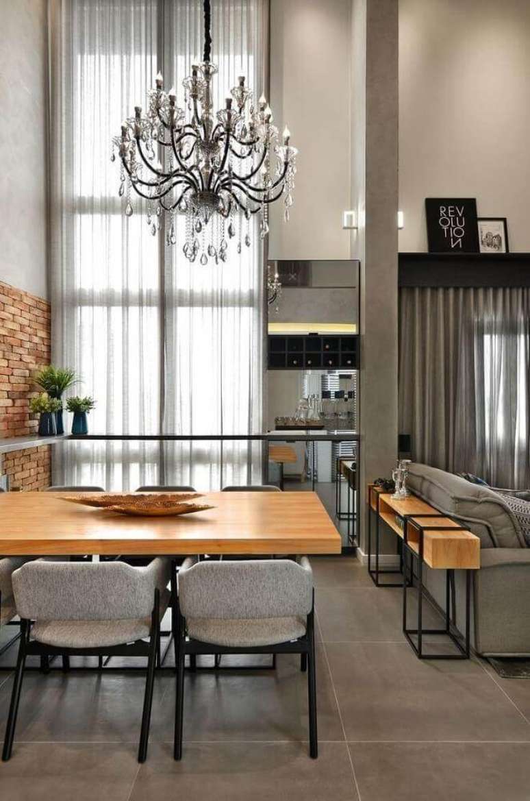 36. Decoração com cadeiras para sala de jantar modernas com mesa de madeira, grande lustre e parede de tijolinho – Foto: Evolukit