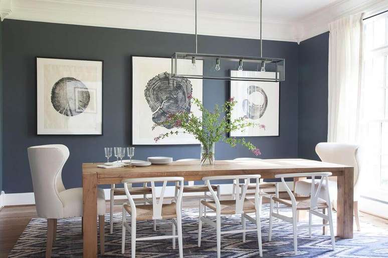 2. Decoração com modelos diferentes de cadeiras para sala de jantar moderna com mesa de madeira e parede com quadros grandes – Foto: Lonny