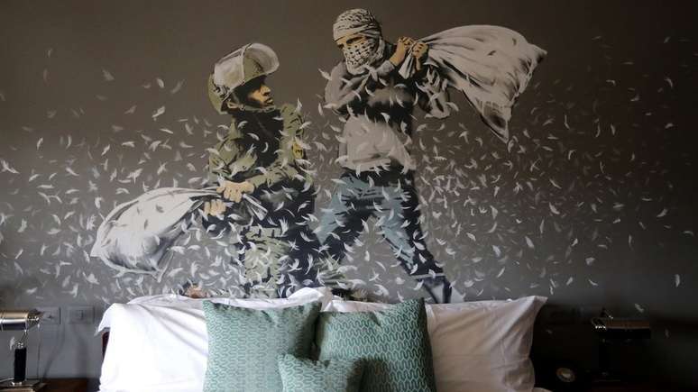 Soldado israelense e militante palestino fazem luta de travesseiro em pintura de Banksy em um hotel criado por ele na Cisjordânia em 2017