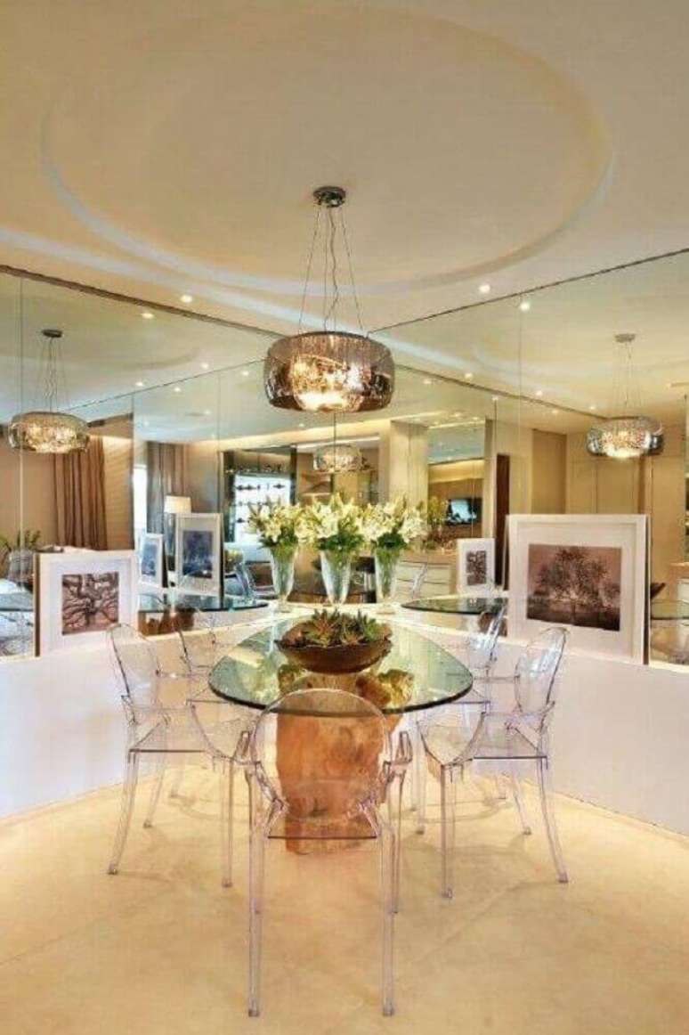 4 Decora&ccedil;&atilde;o com cadeiras de acr&iacute;lico transparente para sala de jantar moderna com paredes espelhadas e base da mesa com tampo de vidro feita em madeira &ndash; Foto: Quitete & Faria