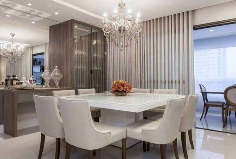 62. Decoração para sala de jantar moderna e sofisticada com parede espelhada e lustre candelabro sobre a mesa – Foto: Vanja Maia