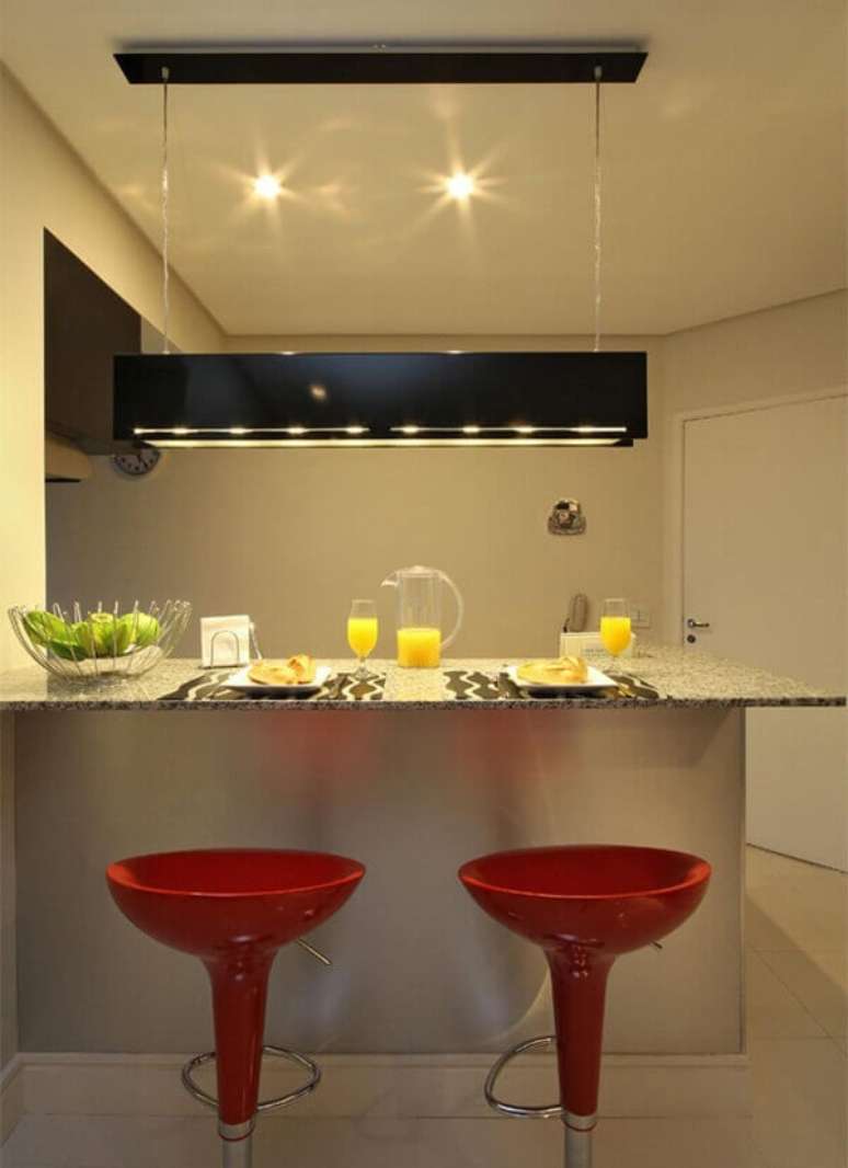 23- O conjunto de luminária retangular e bancada divide os ambientes entre a cozinha americana pequena e a sala de estar. Fonte: 3K Arquitetura e Interiores