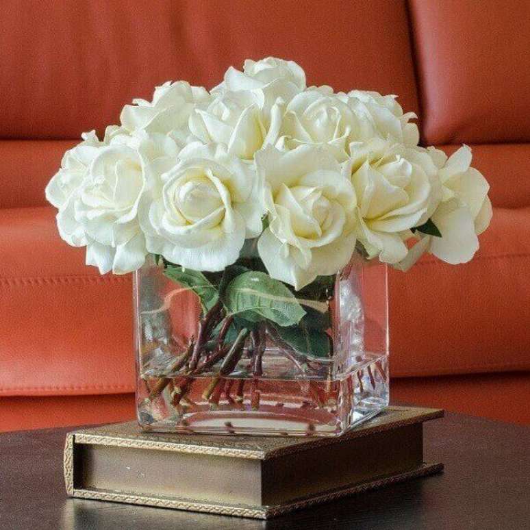 26- O vaso quadrado de vidro transparente tem arranjo de rosas artificiais na cor branca. Fonte: Casa e Festa