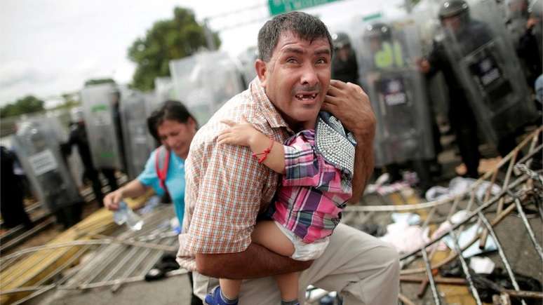 Hondurenho protege o filho após rompimento das grades da fronteira do lado da Guatemala