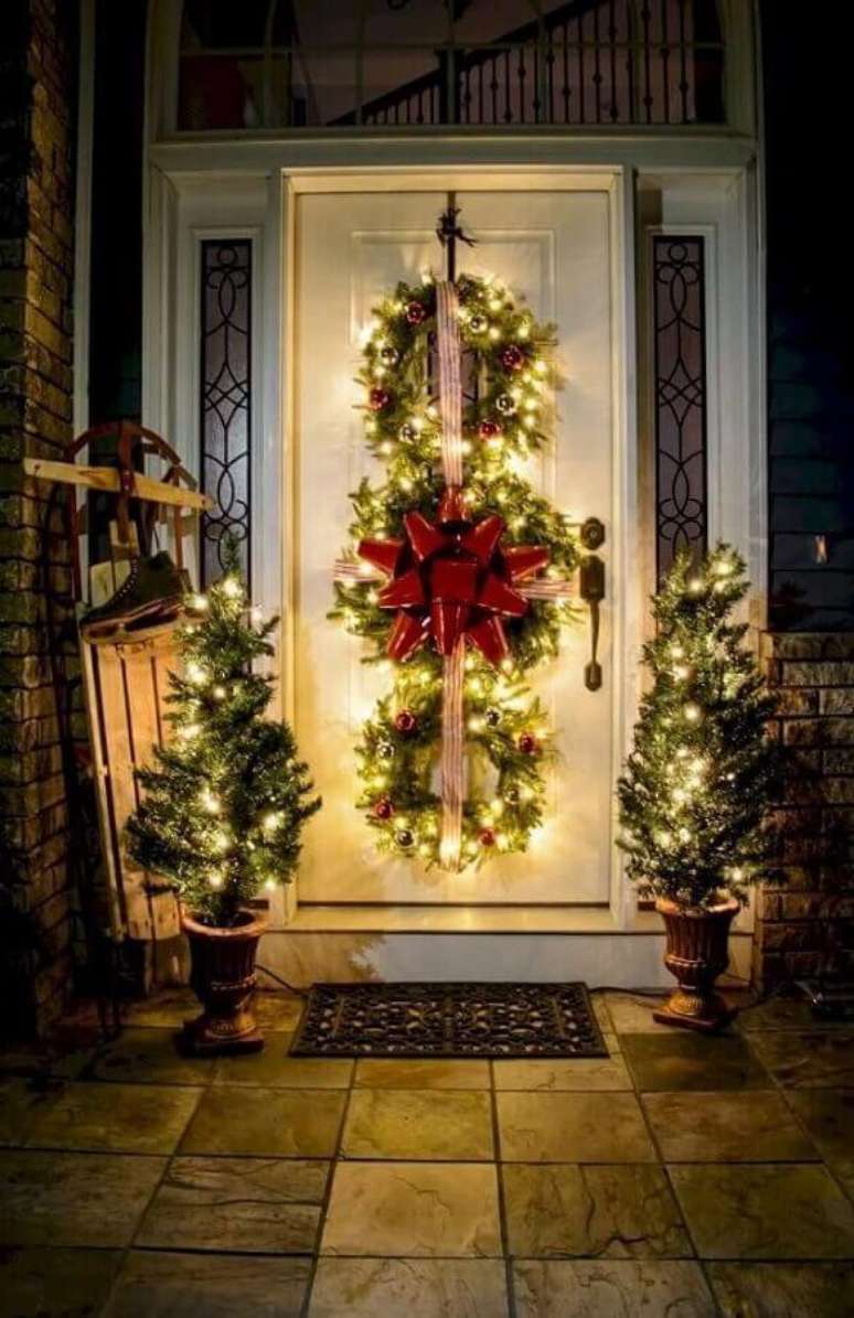 20. Linda decoração com luzes de natal para área externa decorada com dois pinheiros pequenos e guirlandas na porta – Foto: Roomodeling