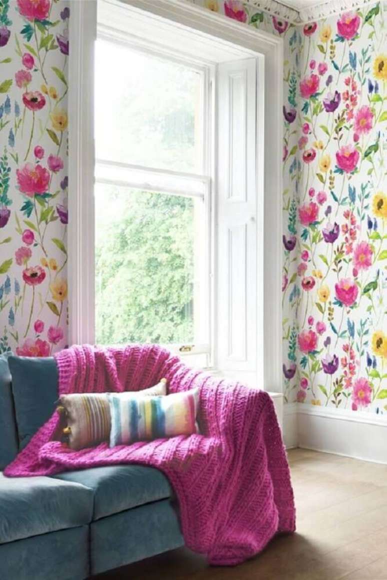 50. Decoração para sala de estar com sofá azul e papel de parede com flores coloridas – Foto: Pinterest