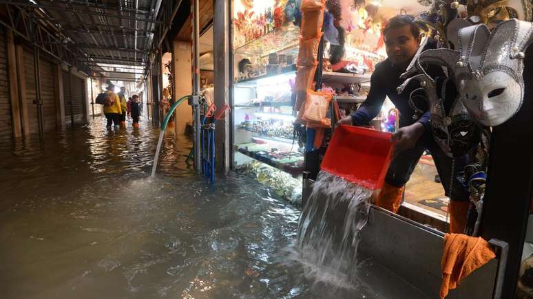 Lojista tenta proteger suas mercadorias em centro comercial tomado pela &aacute;gua