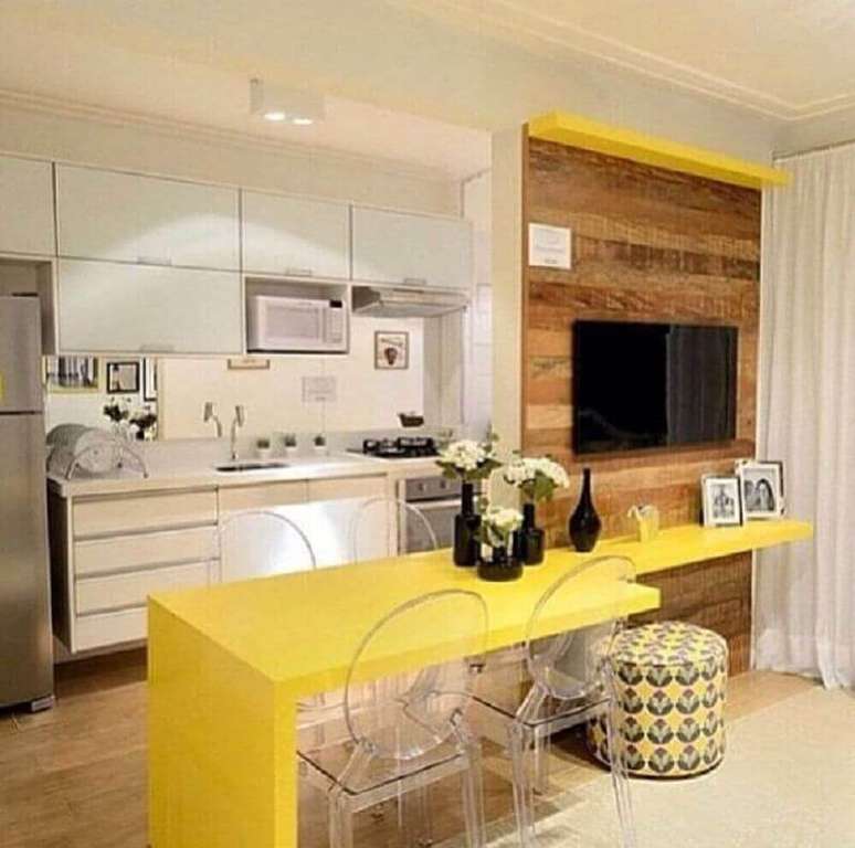 15. Decoração com bancada amarela e cadeiras de acrílico transparente para cozinha americana com sala de estar integrada – Foto: The Holk