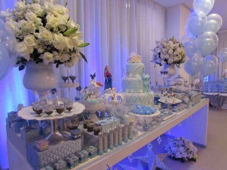 49- A iluminação azul sob a mesa complementa a decoração da festa Frozen ideias criativas. Fonte: Mães Comadres