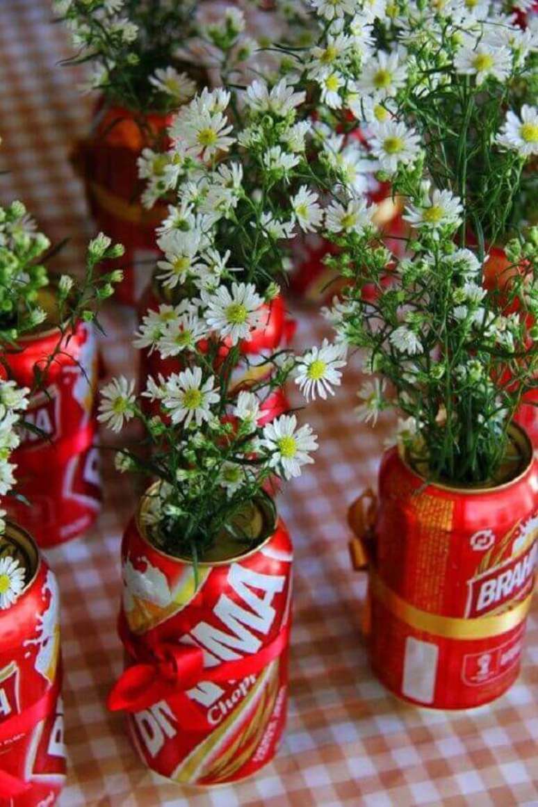 39- Na festa de boteco os centros de mesa com flores utilizam latas de cerveja com laços de fita. Fonte: Casandinho