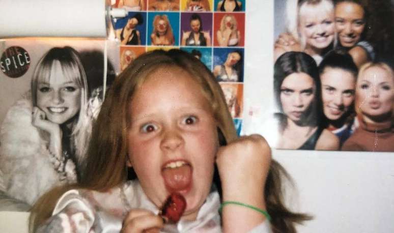 Adele em sua infância ao lado de pôsteres das Spice Girls.