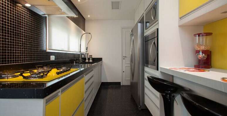 55. No ambiente as cores pretas e amarelas das pastilhas para cozinha revestem a parede e combinam com os m&oacute;veis. Fonte: BBel
