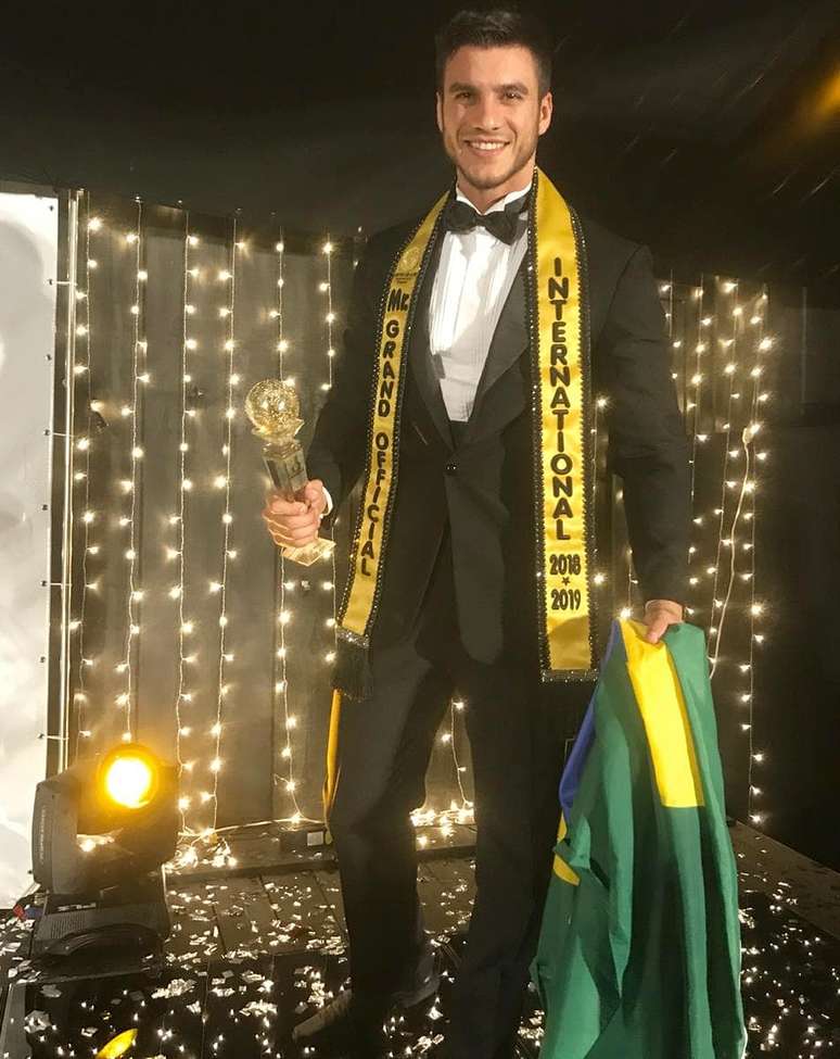 O novo Mister Grand International com o troféu e a bandeira do Brasil: triunfo sobre competidores de vários países