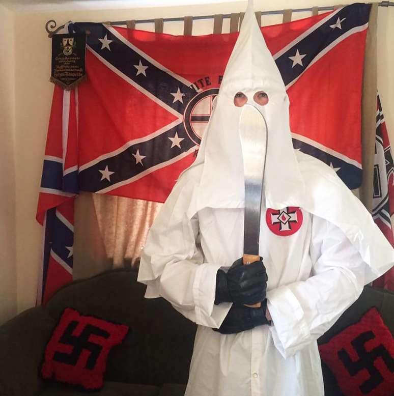 Thomas segura um facão vestido com o traje característico da Ku Klux Klan