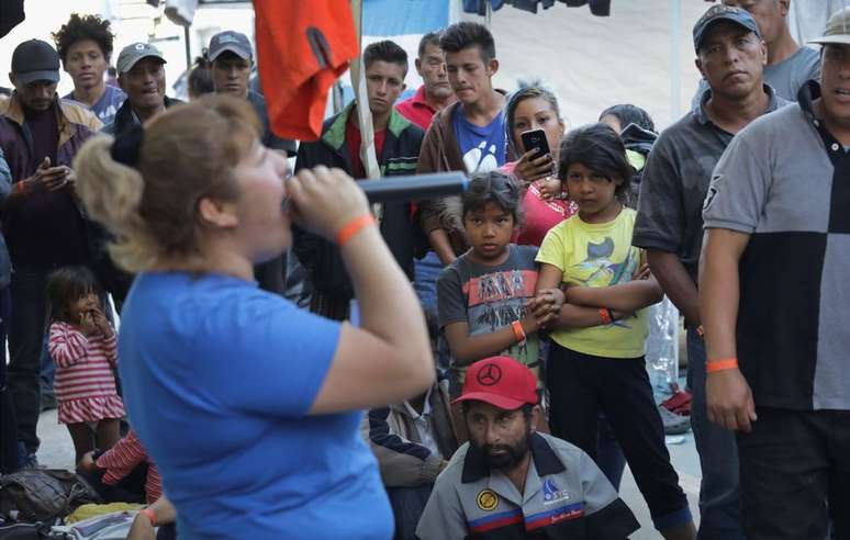 Um grupo de migrantes observa uma mulher cantando no karaokê no abrigo improvisado
