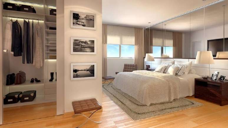 55. Modelo de quarto de casal com closet pequeno decorado com piso de madeira e parede espelhada sobre a cama – Foto: Estéfany Furtado