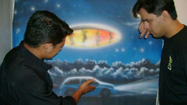 O jornalista Genito mostra um quadro que pintou, baseado na experi&ecirc;ncia que relata ter tido com &oacute;vnis - no quadro, uma nave oval brilhante sobrevoa um carro