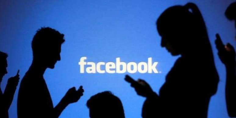 Pessoas utilizam celulares diante de projeção do logo do Facebook em foto ilustrativa