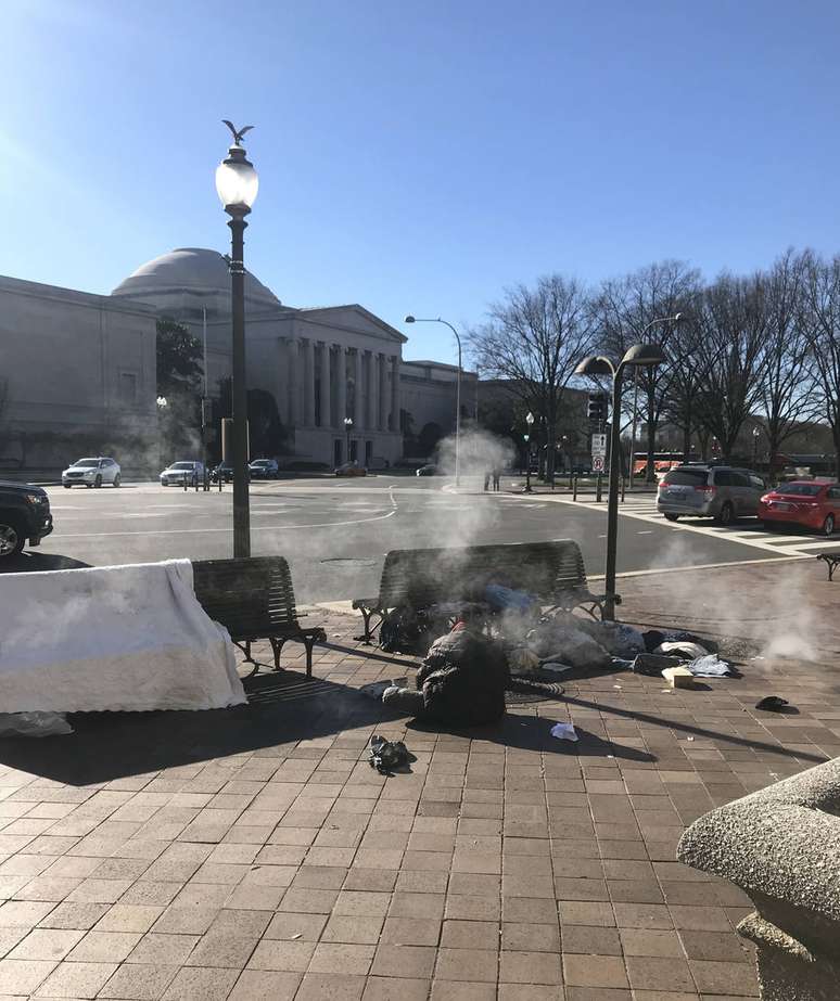 Morador de rua se protege do frio próximo à saída de ar de bueiros, na Avenida Pensilvânia, a 1 quilômetro do Capitólio, em Washington