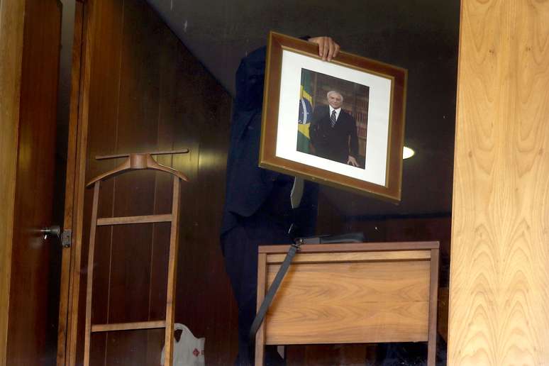 Funcionário retira da parede um quadro com a foto do ex-presidente Michel Temer de uma sala no quarto andar do Palácio do Planalto, em Brasília, nesta quarta-feira (2)
