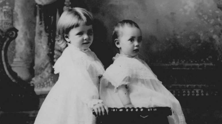 Menina e seu irmão bebê usando vestido branco; fotografia de 1905, nos Estados Unidos