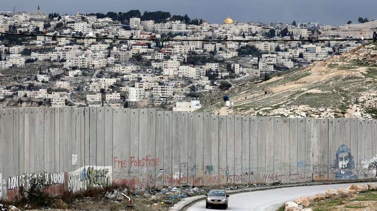 Carro passa por muro israelense na cidade palestina de Abu Dis, com Jerusalém ao fundo; historicamente, Brasil mantém posição neutra no conflito