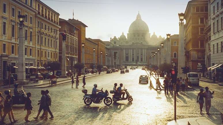 Vista geral do Vaticano no pôr do sol, com pessoas e motos em primeiro plano